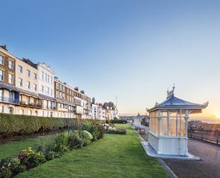 Ramsgate West Cliff white shelter in front of flower beds with the sun rising over the harbour