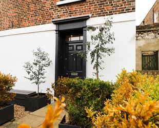 Black front door to Margate Cottage with paved path and plant pots