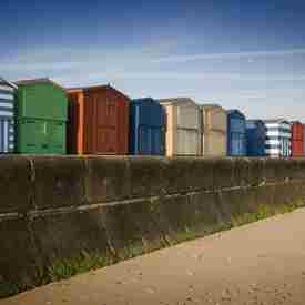 Row of coloured beach huts on promenade  above sandy beach and bright blue sky behind