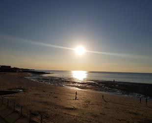 Sunset over West Bay with sun reflecting on sea with people on beach  