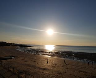 Sunset over West Bay with sun reflecting on sea with people on beach