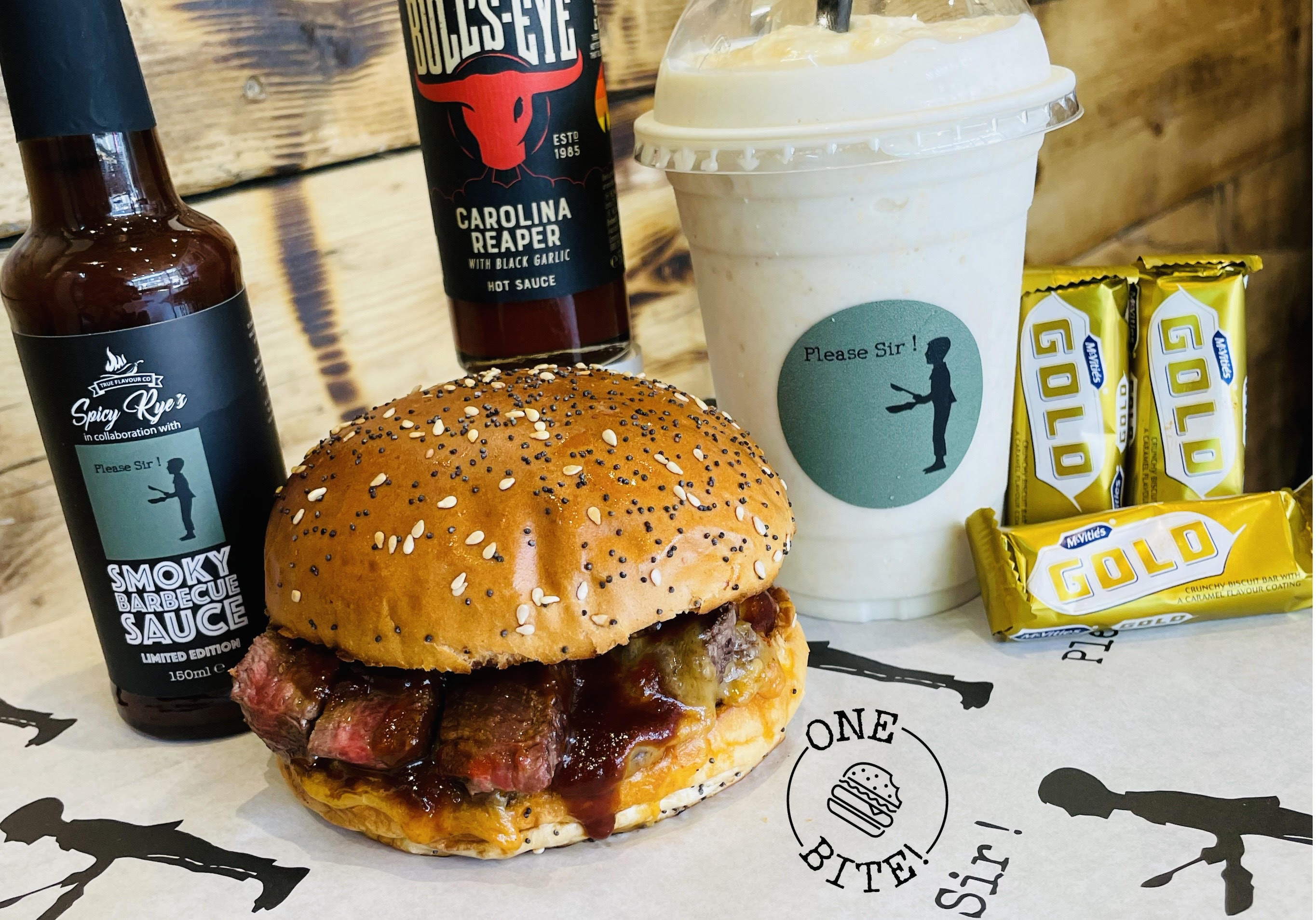 Burger, white coffee cup, chocolate bar packs and bottles of sauce