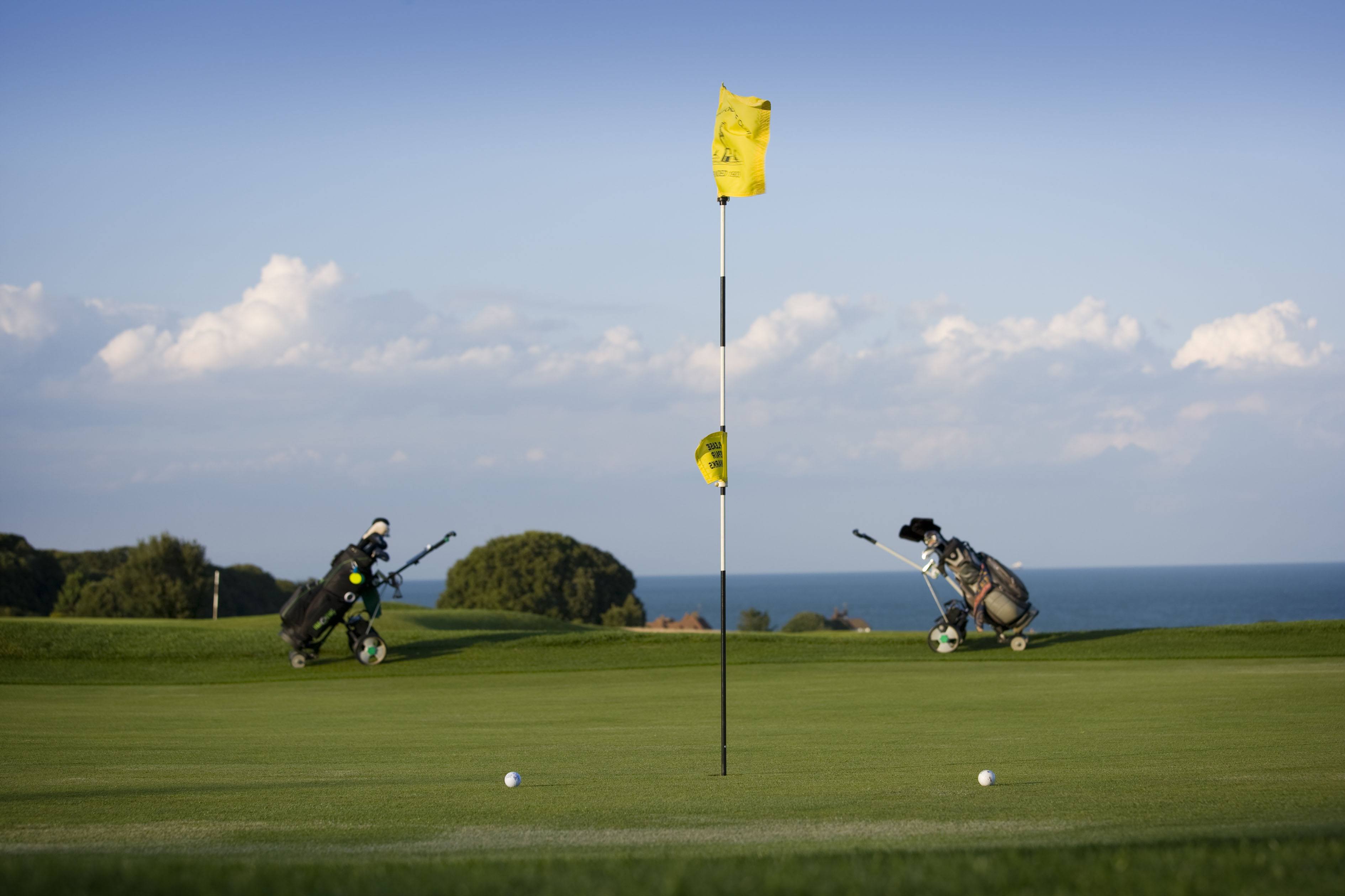 Golf flag in hole with a golf bag either side. Sea in the background