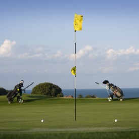 Golf flag in hole with a golf bag either side. Sea in the background