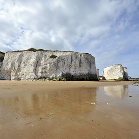 White chalk cliffs and stack set back from sandy beach. Grass on top of cliffs.Bright blue sky
